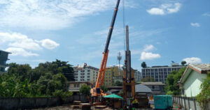 หน้างานเสาเข็มเจาะกลางชุมชน มีเครนและปั้นจั่นทำงานติดอาคารข้างเคียง
